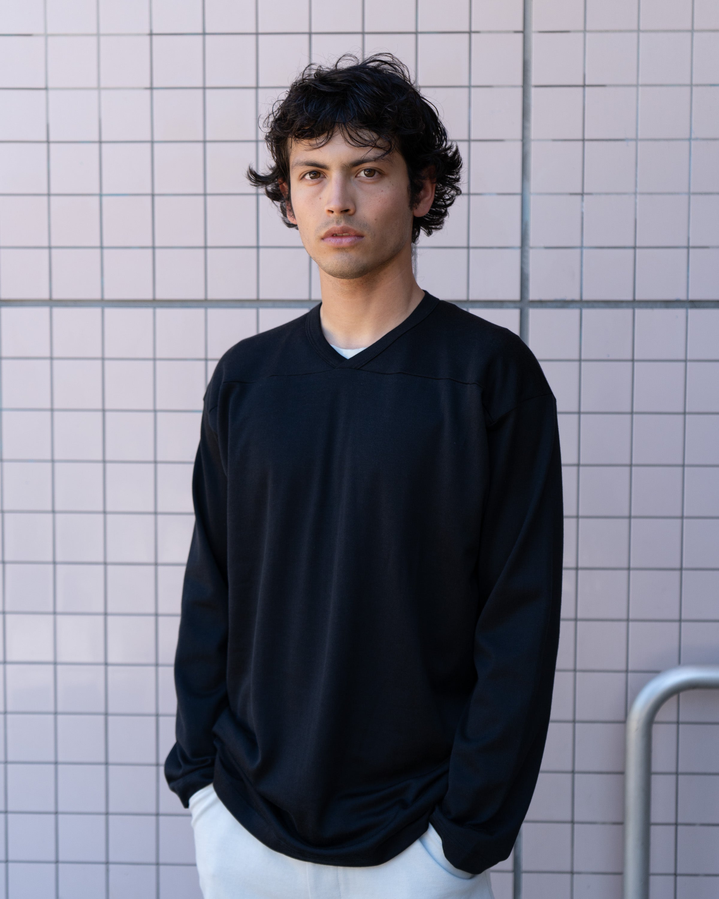 Model wears a LW135 LS Football T-shirt in Black against a tiled stone background