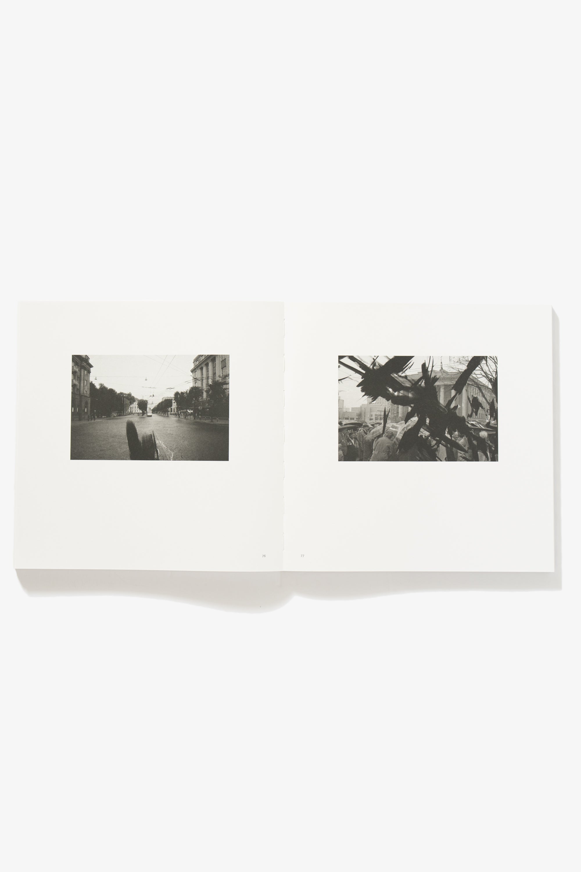 Spread of Grey But Not Grey. Verso shows a street scene, empty paved road, a bus in the distance. Recto shows a street scene of pedestrians, the view of them obscured by an indeterminate metallic structure