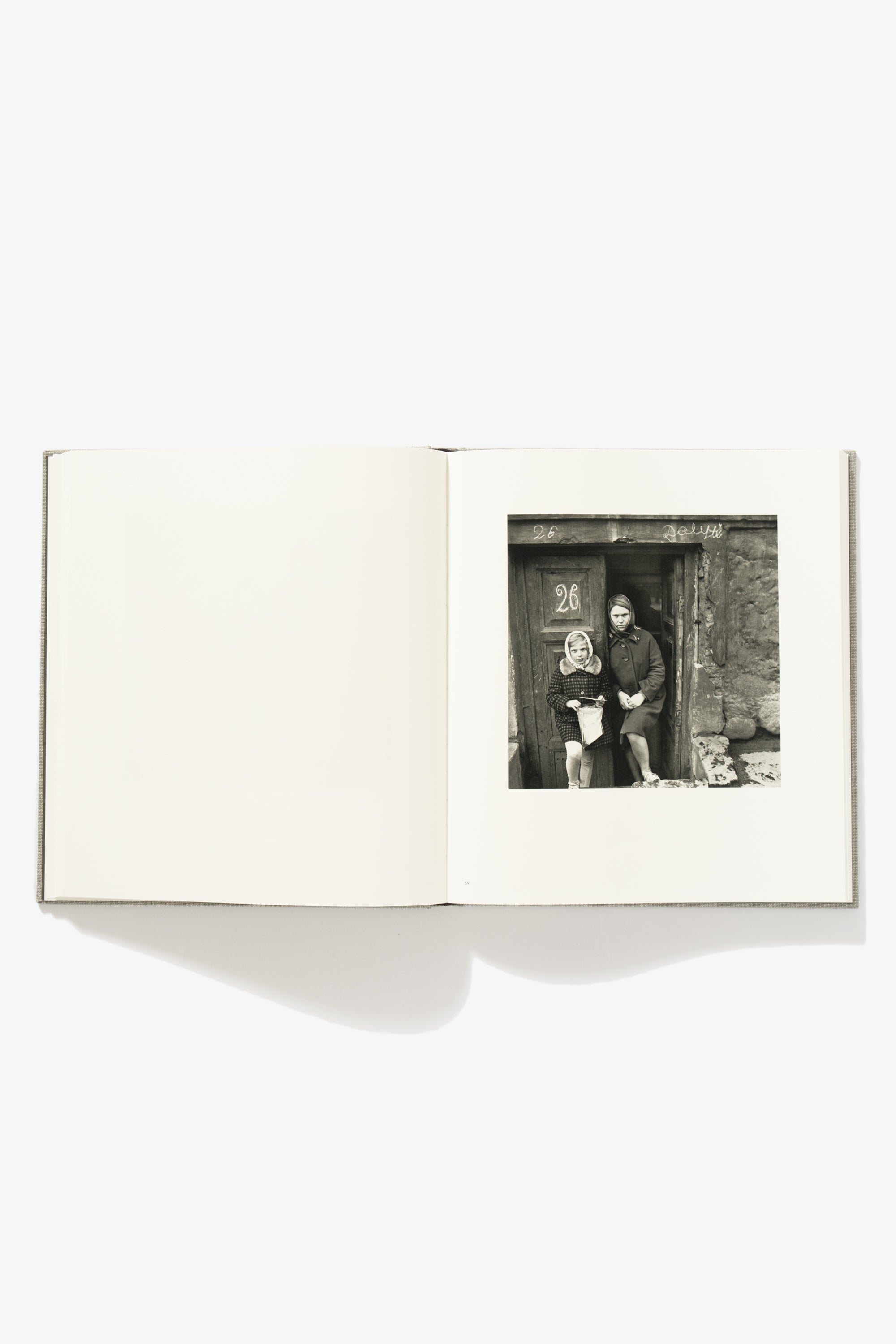 Spread of People of Lithuania. Verso is blank. Recto shows two girls standing in the doorway of a half-basement dwelling. The number “26” is painted on the door.