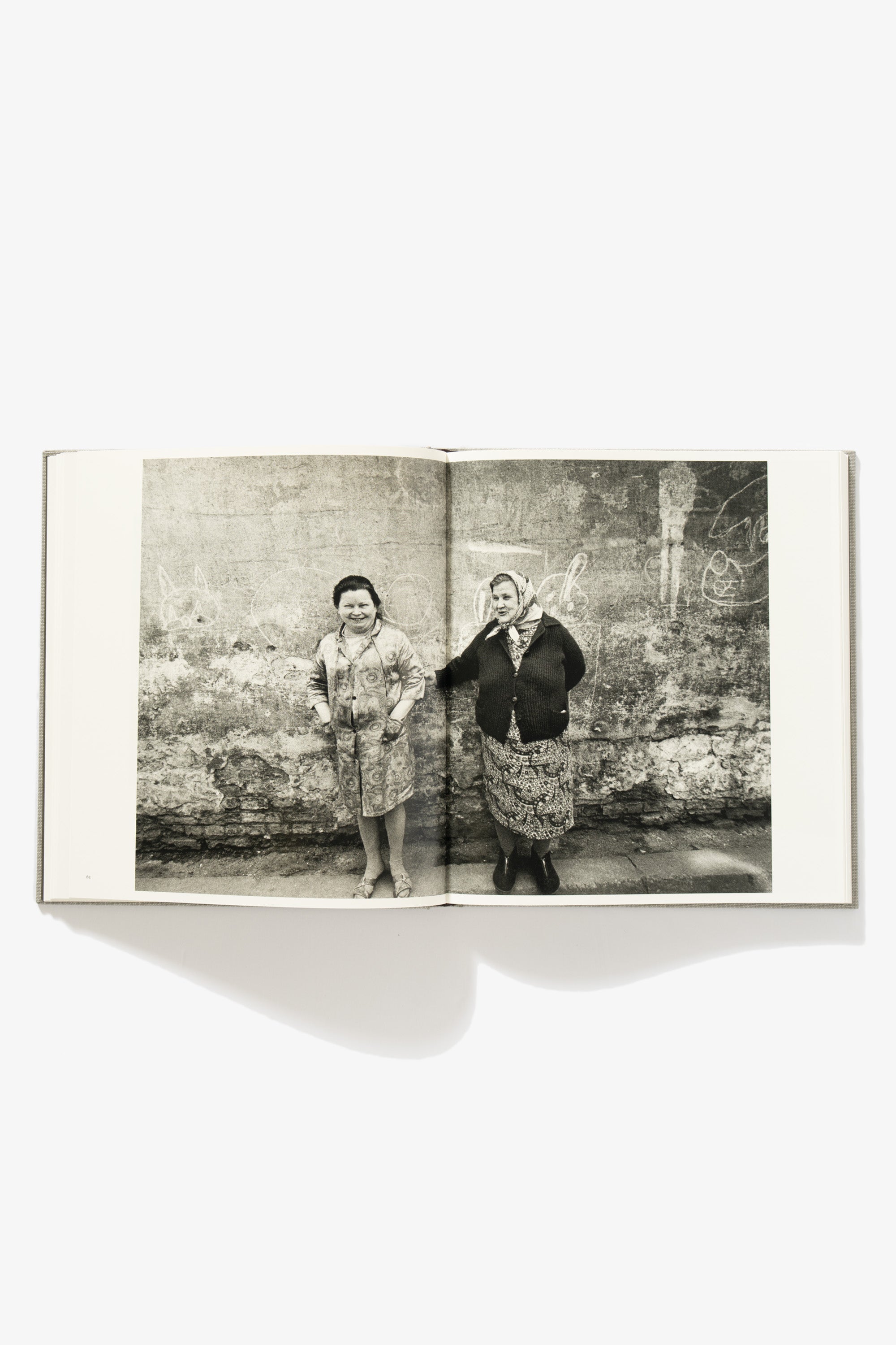 Spread of People of Lithuania. Two-page spread. Verso shows a woman smiling, standing against a textured gray wall. Recto shows another woman standing against the same wall, one arm extending to the first.