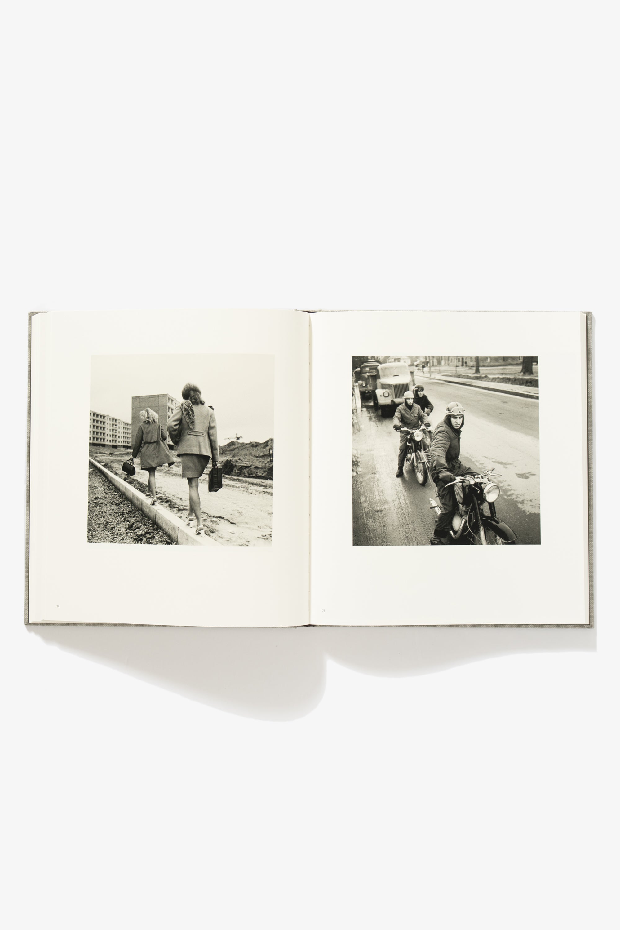 Spread of People of Lithuania. Verso shows two women walking along a low retaining wall set into beachy sand, their shoes in their hands. Recto shows a line of traffic, with three men on motorcycles looking up into the camera. 