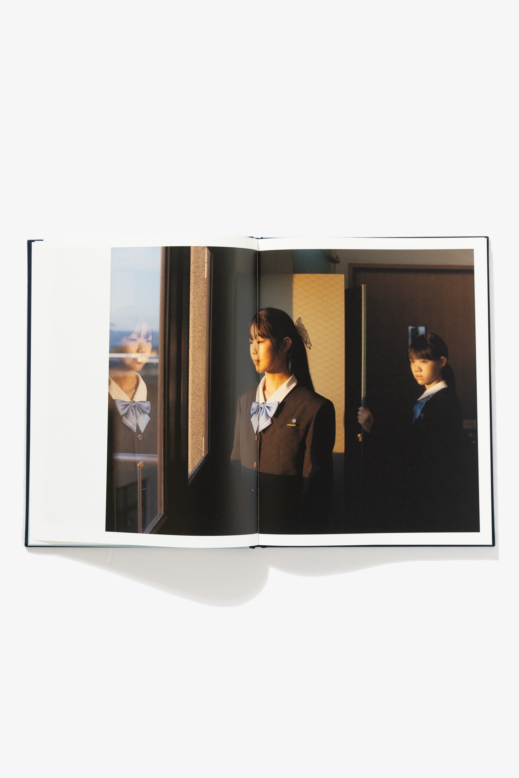 Spread of Goodbye Blue Spring. Image occupies both pages. A school girl looks out of a window, the light from a setting sun on her face. Another girl stands behind her, her gaze indeterminate, holding a pool cue.