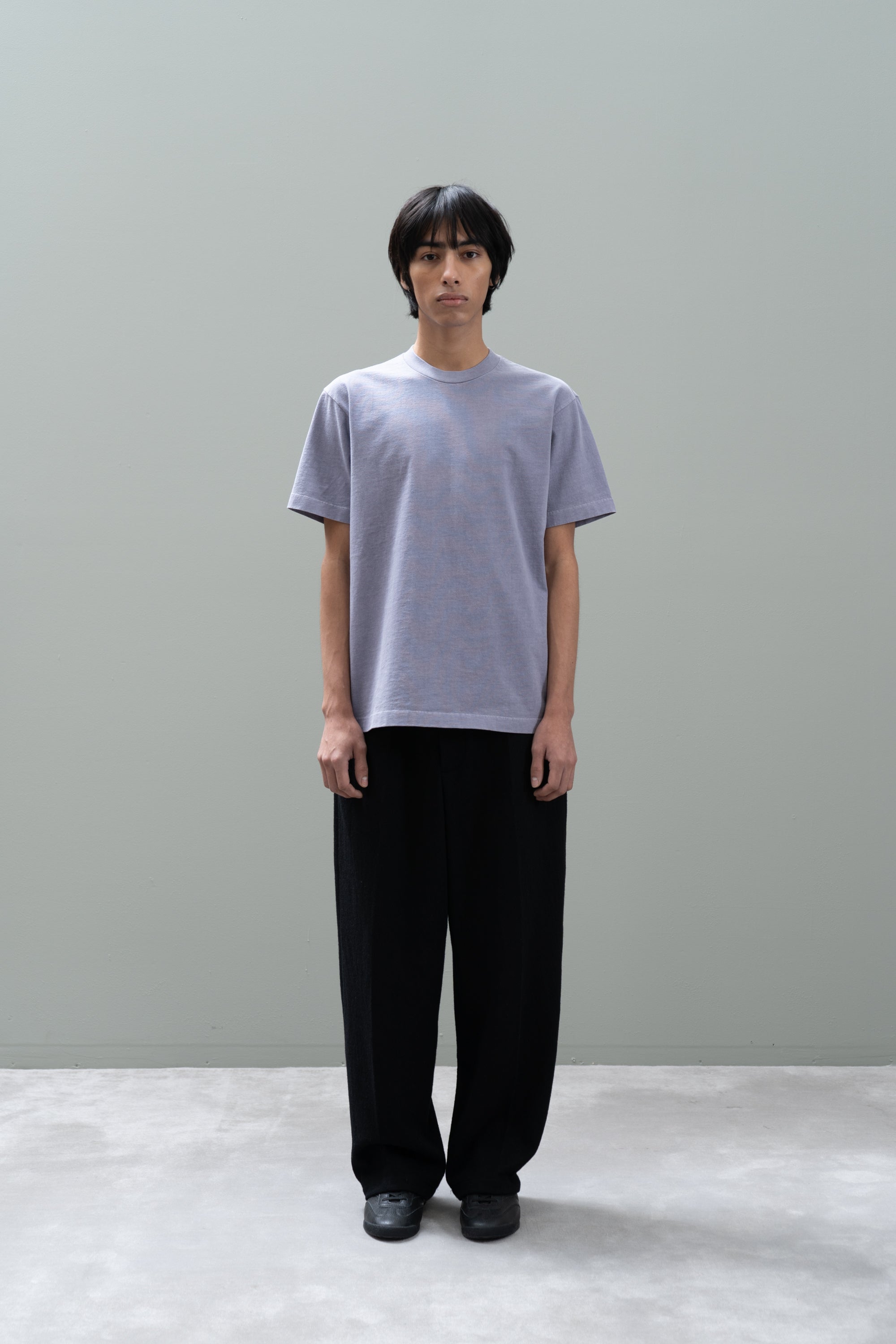 Person wearing a light gray t-shirt and black pants against a plain background