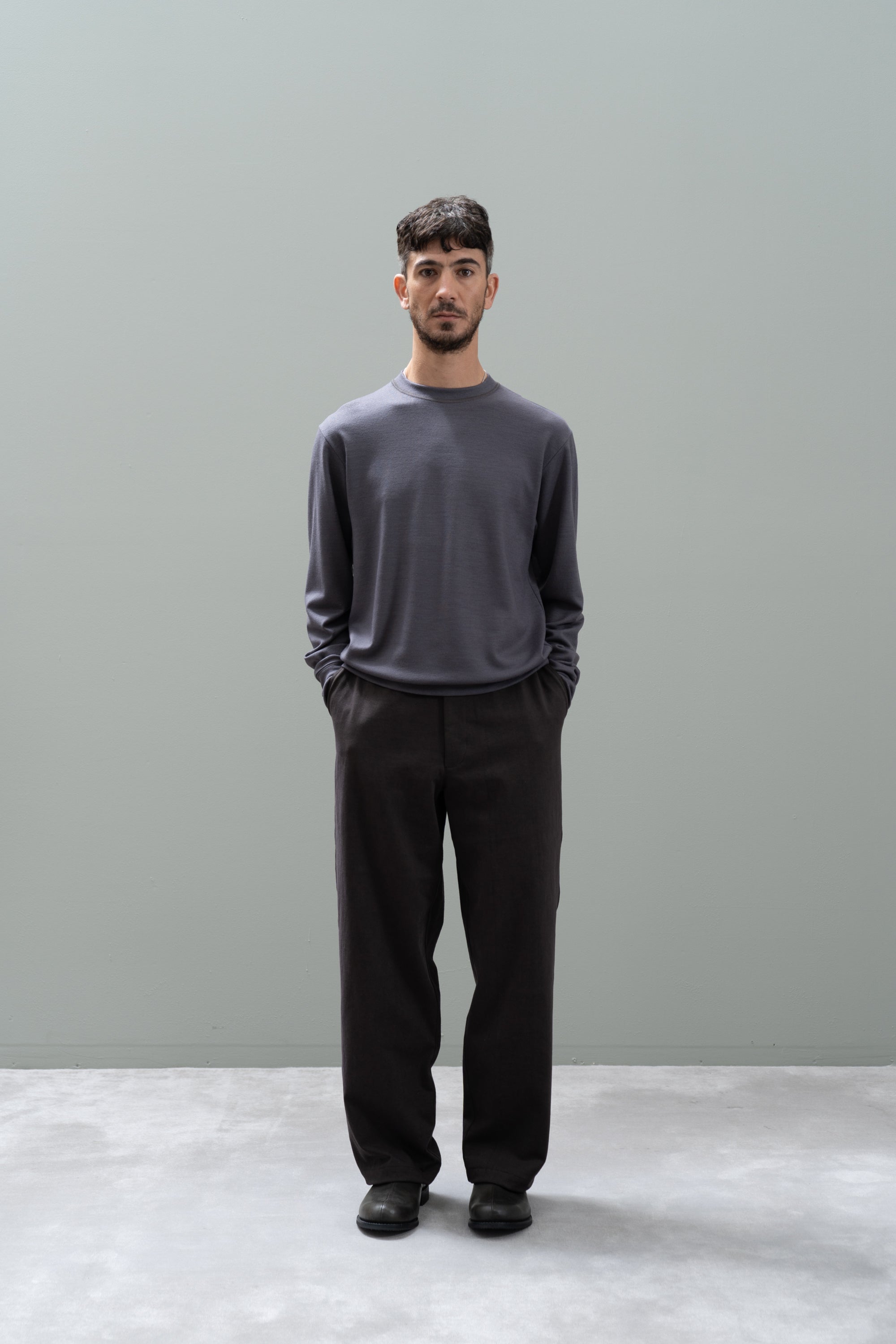 Man wearing a gray sweater and black pants against a plain background