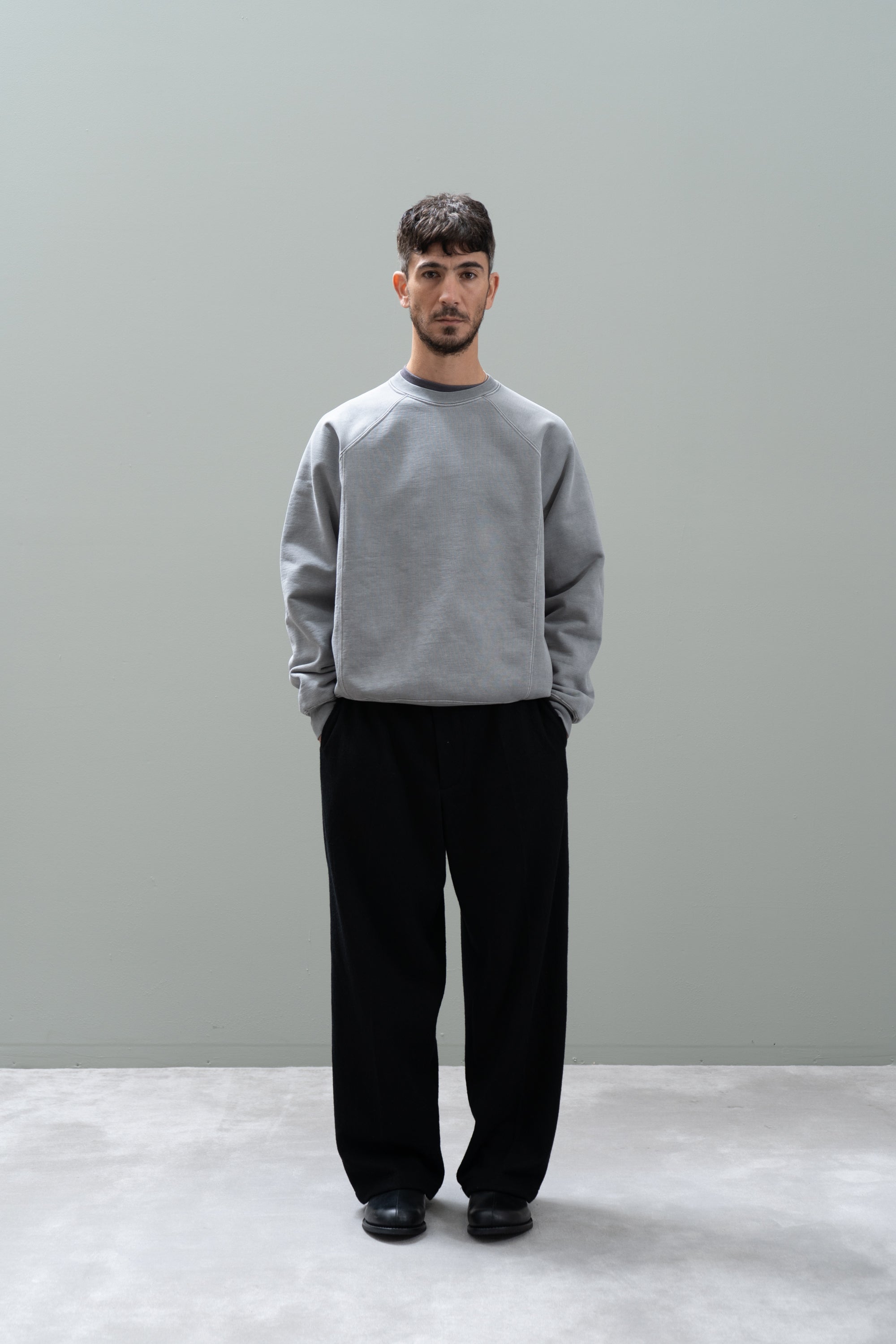 Person wearing a gray sweatshirt and black pants against a plain background