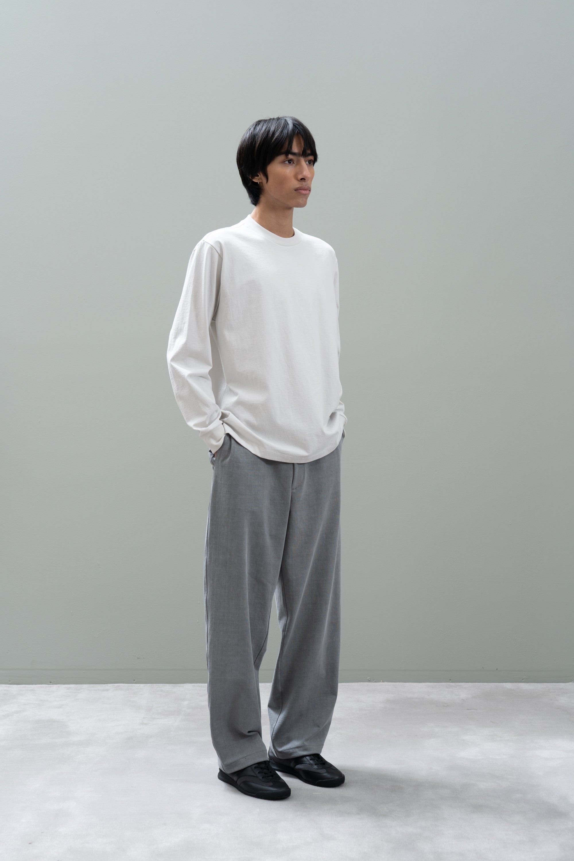 Person wearing a white shirt and gray pants against a plain background
