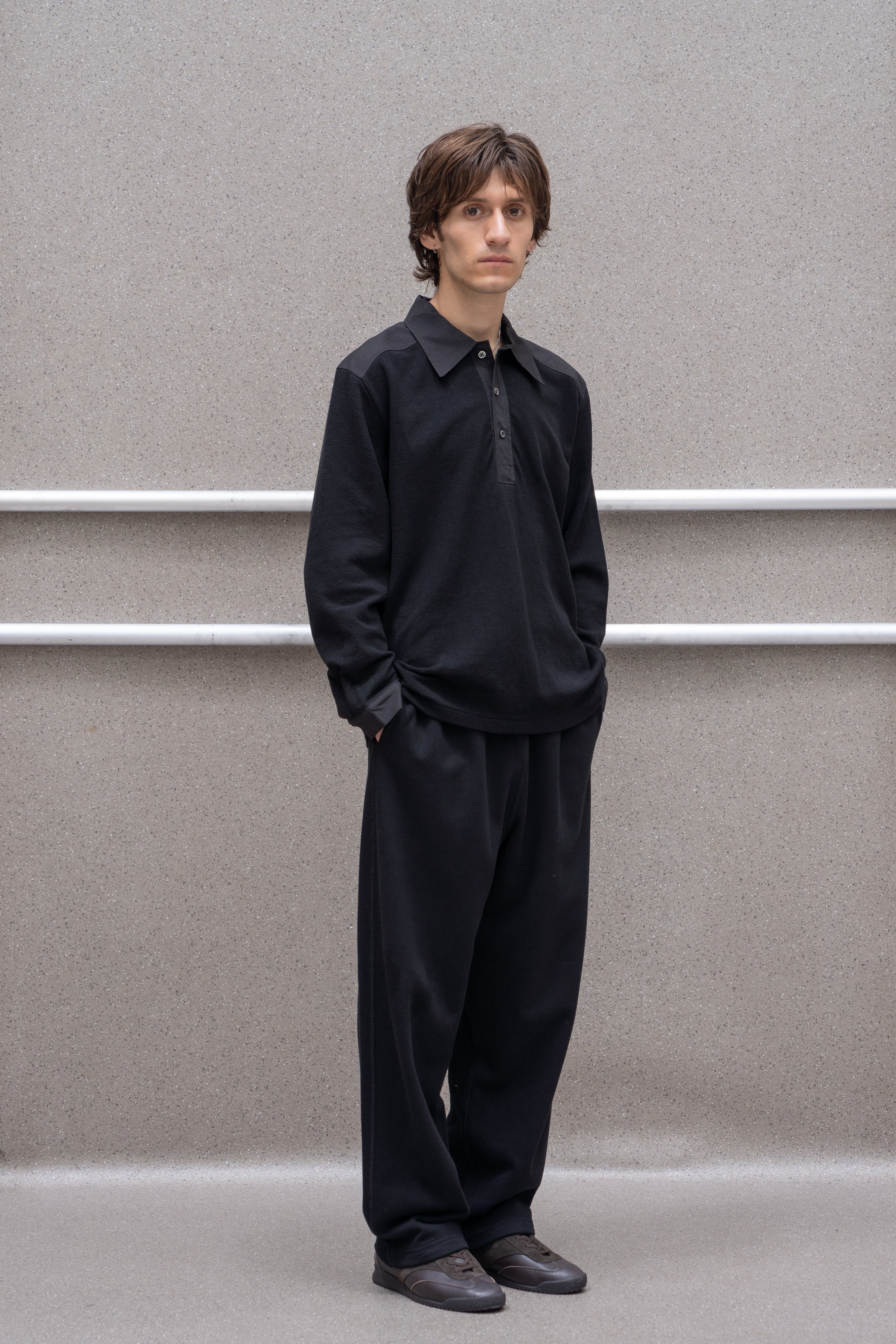A model wears the LW415CL Double Knit Polo in Black against a grey background, askew from the direct sight line of the camera
