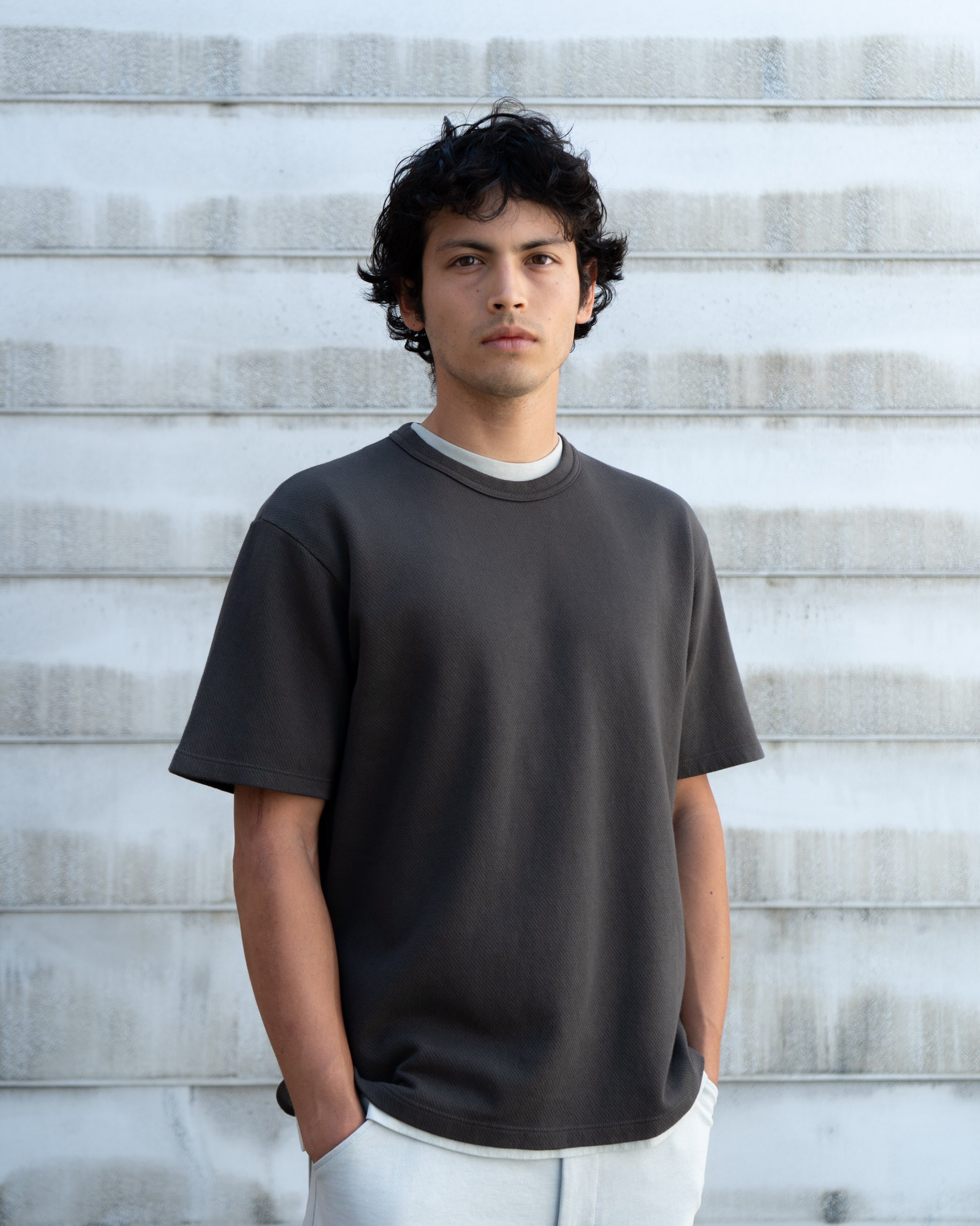 Model wears a LW134T Mesh T-shirt in Black Pine against a corrugated metal background