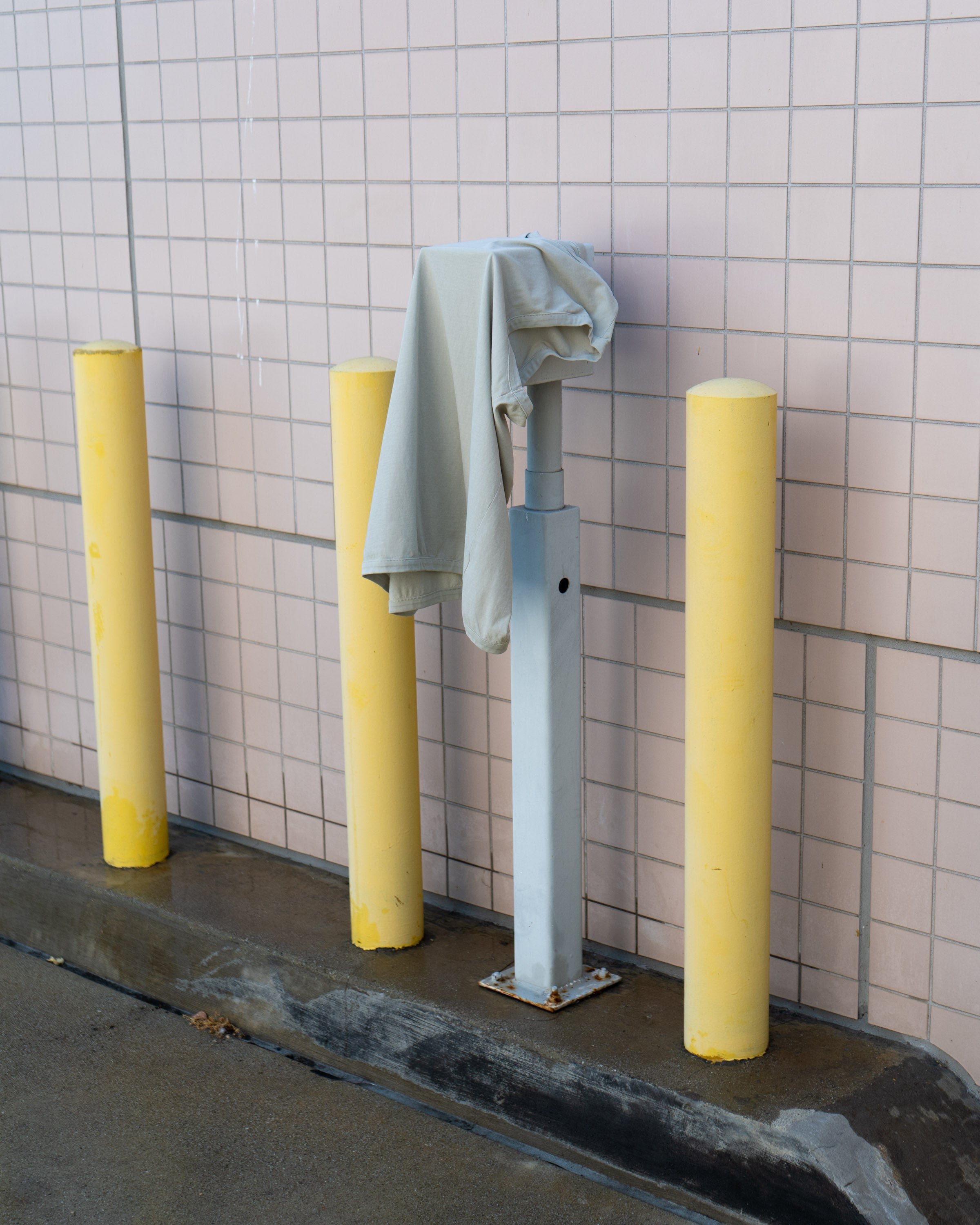 LW106 Sleeveless T-shirt hung over a post, surrounded by yellow post, against a tiled background