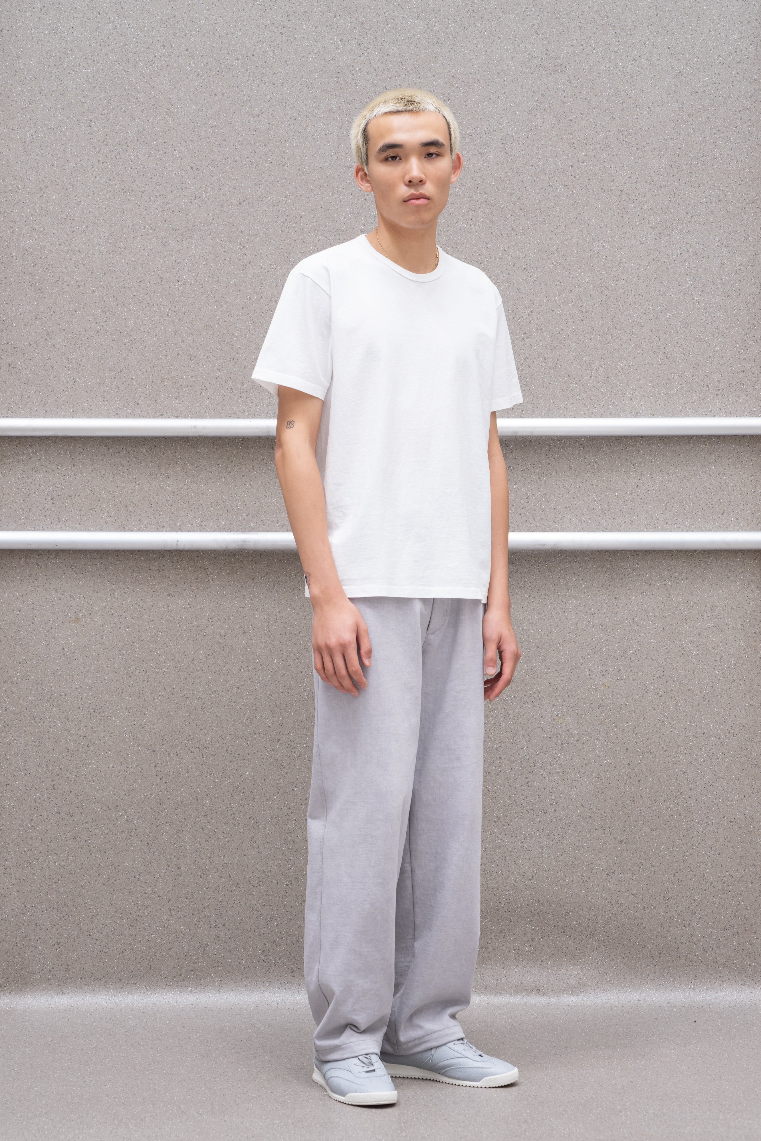 A model wears a LW101 "Our T-shirt" in white against a grey background, askew from the direct sight line.