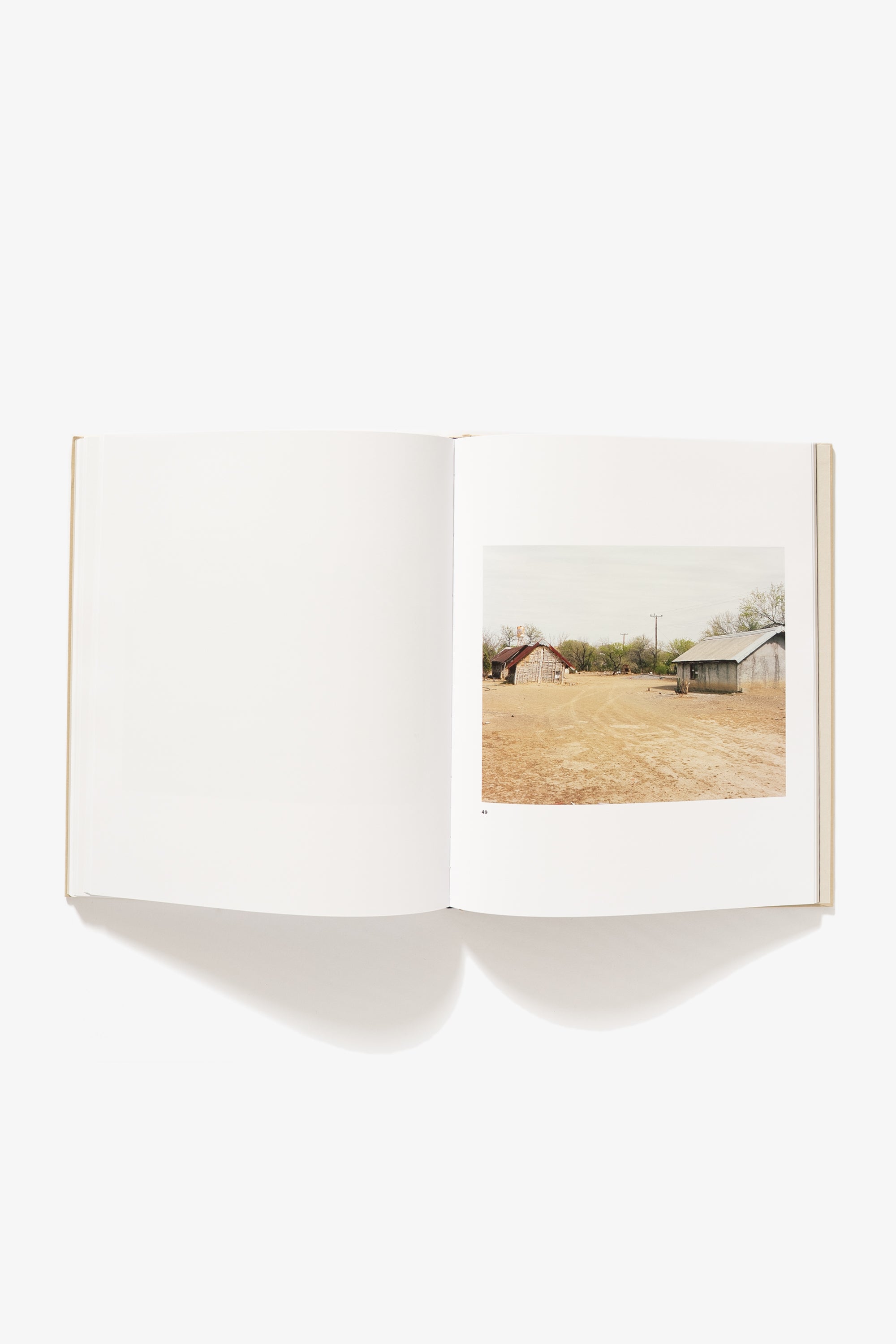 Spread from Felipe Romero Beltran's "Bravo." Verso is blank, recto is a landscape of two roofed structures set diagonally across from each other on a barren grass field.