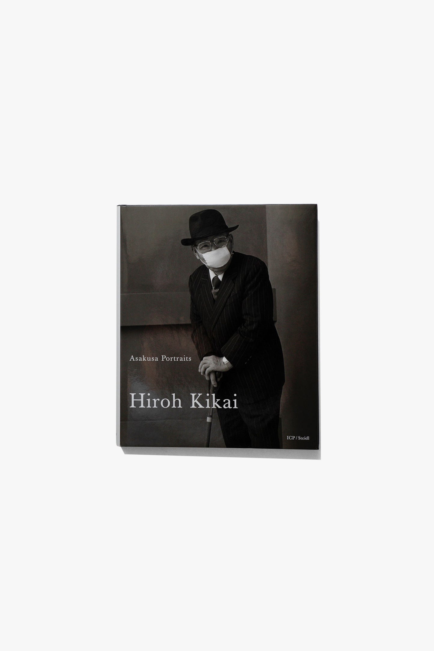 Book cover of Hiroh Kikai's "Asakusa Portraits." Portrait of an older man in a suit and top hat, wearing a face mask, leaning on his cane. 