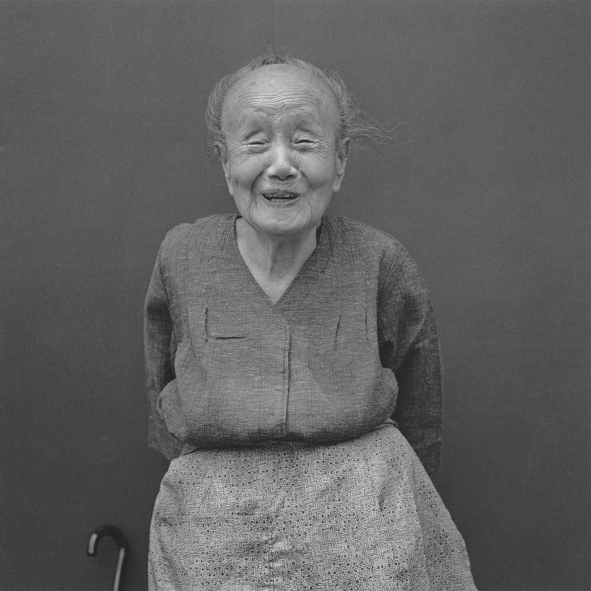 Photograph from Hiroh Kikai's "Asakusa Protraits." Portrait of an elderly woman standing against a plain background.
