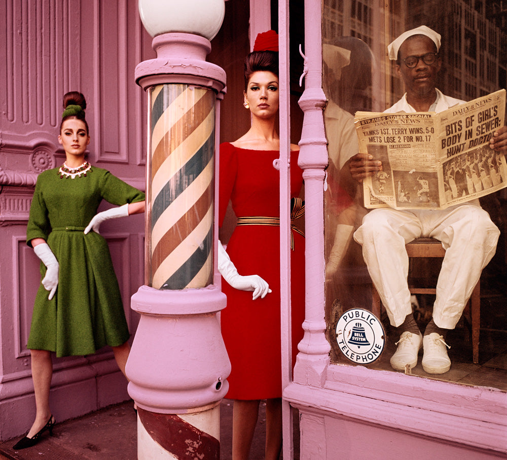 An outtake from William Klein's photograph in 1962 for Vogue. Two women models pose between a barbershop pole. A man seated inside the adjacent window reads a newspaper. The headline reads "BITS OF GIRL'S BODY IN SEWER: HUNT DOCTOR." 