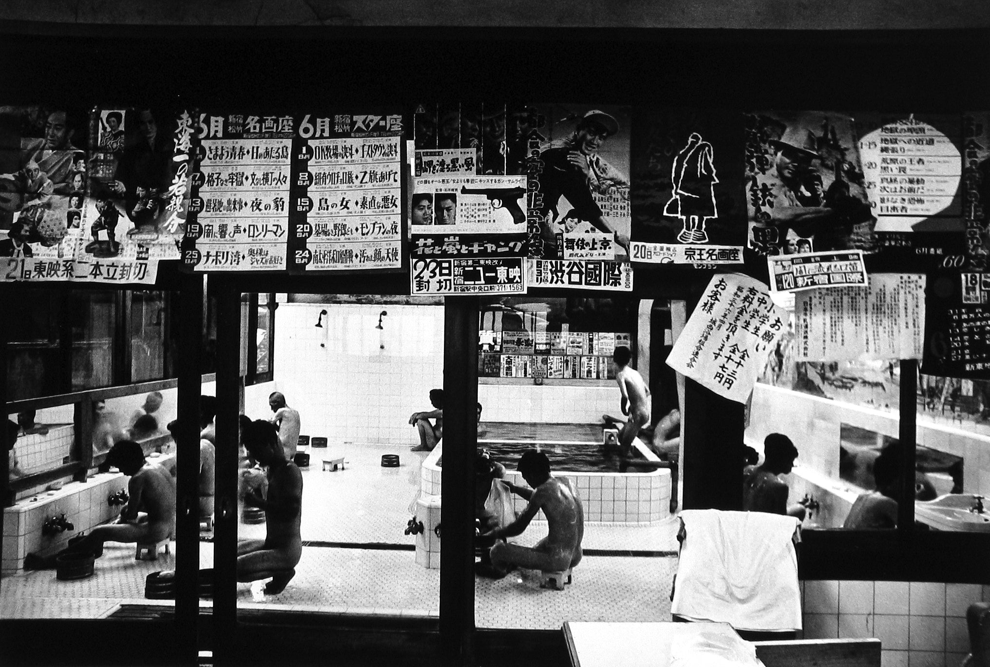 Image from William Klein's Tokyo 1961. Men wash and lounge in a public bath in Japan, a curtain of advertisements above them. 