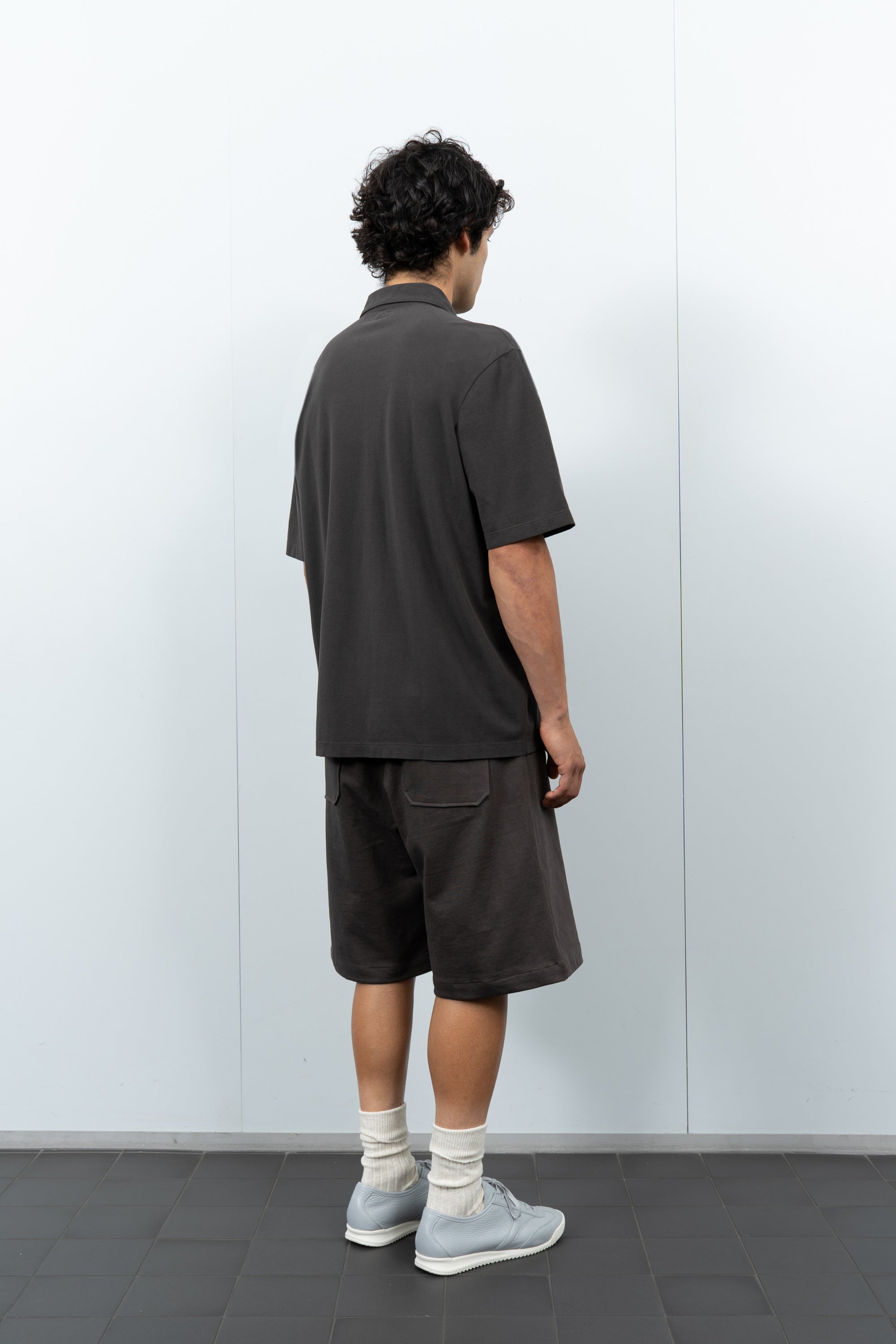 quarter-turn rear-facing on-model photograph of model wearing LW400 Pique Two Button Polo in Black Pine