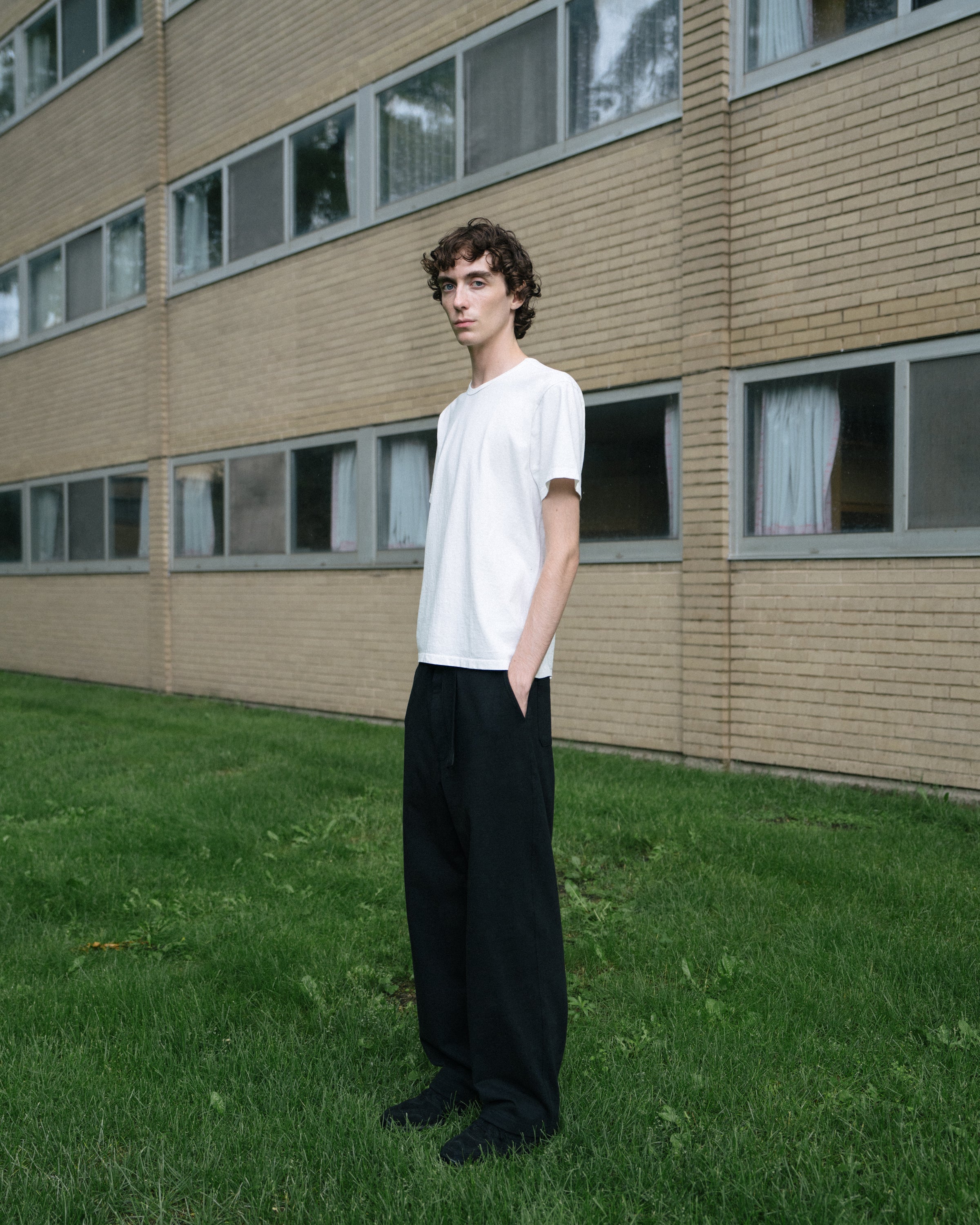 Model wears a white LW101 "Our T-shirt" on a grass field outside of S.R. Crown Hall.