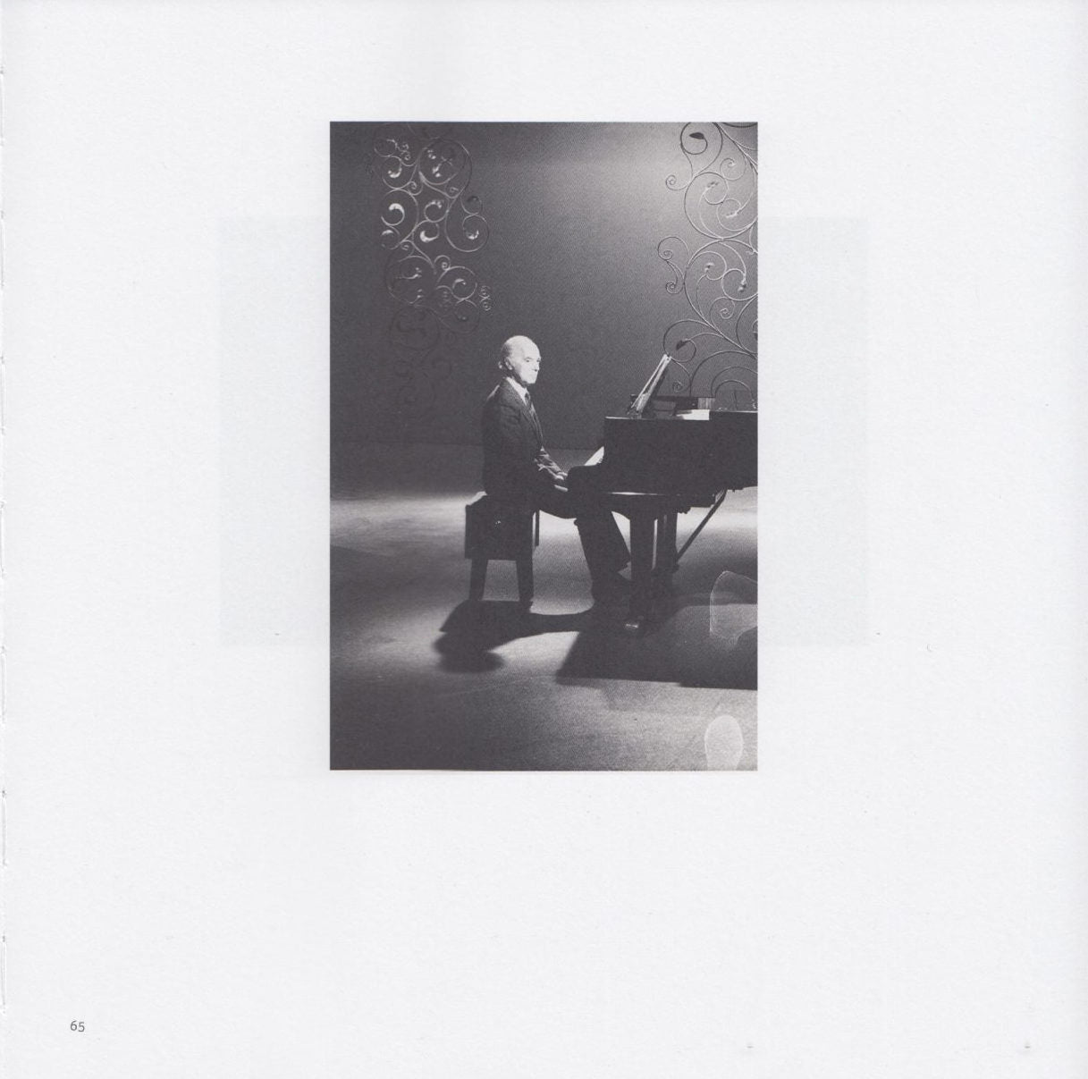 Photograph from Anton Seskus. A man sits at a piano with decorative structures in the background and foreground.