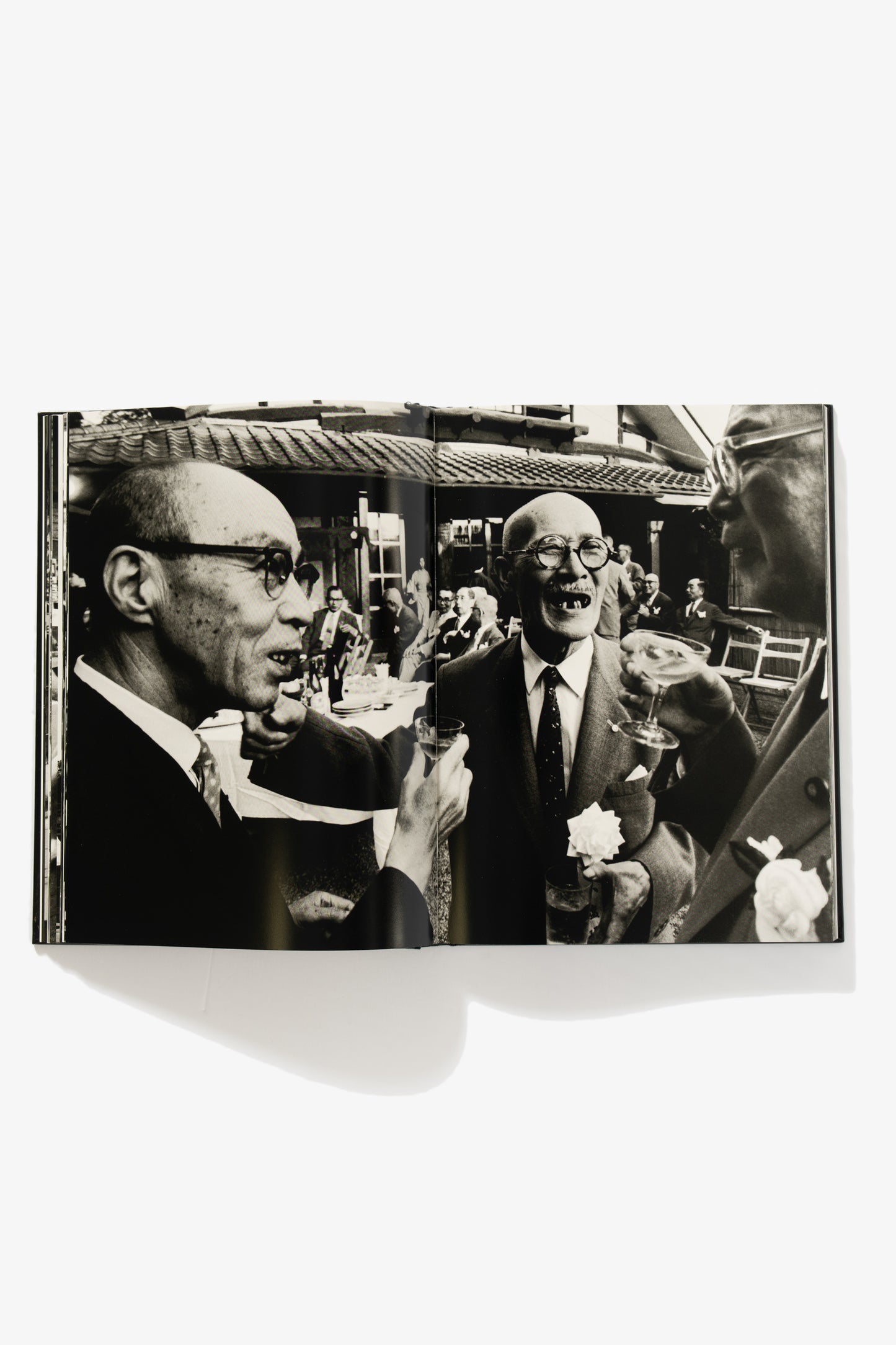 Spread of Tokyo 1961. One image occupies both pages, a close-up of older men in suits chatting with drinks. One man’s missing teeth feature prominently on his face.