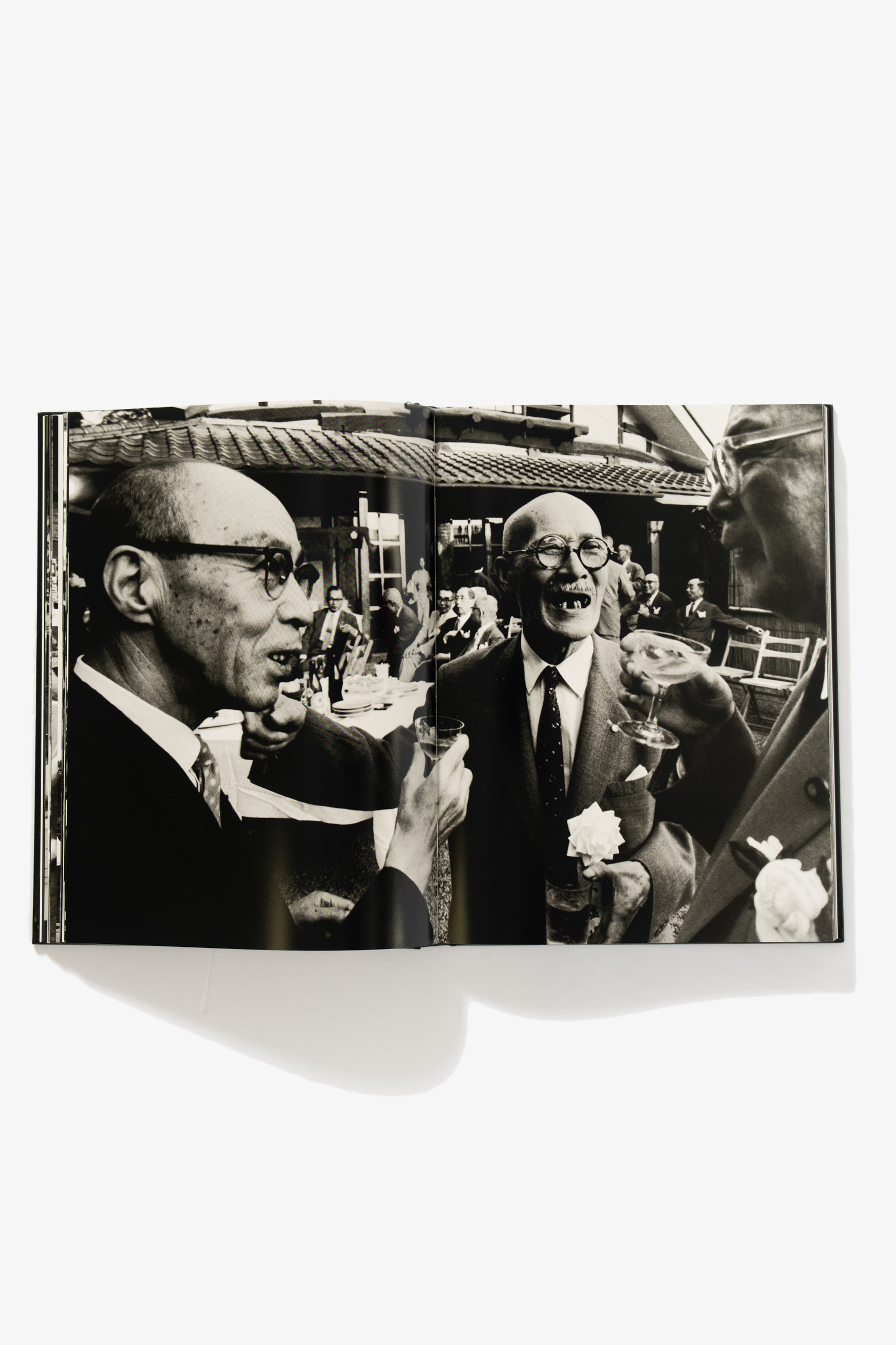 Spread of Tokyo 1961. One image occupies both pages, a close-up of older men in suits chatting with drinks. One man’s missing teeth feature prominently on his face.