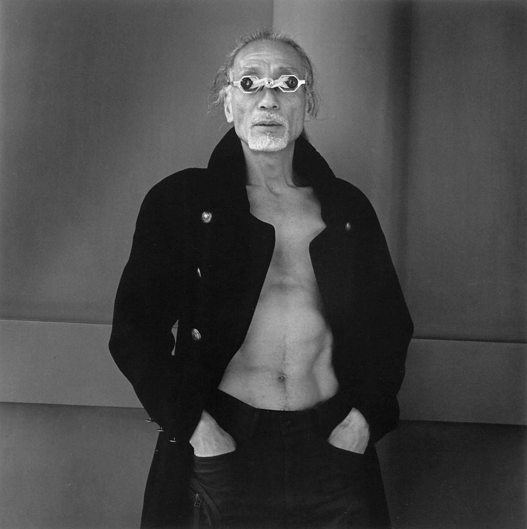 Photograph from Hiroh Kikai's "Asakusa Protraits." Portrait of a man wearing a dark coat with no shirt underneath, with an interesting pair of sunglasses. 