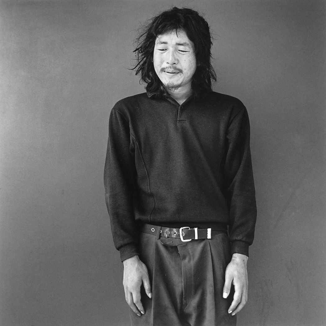 Photograph from Hiroh Kikai's "Asakusa Portraits." Portrait of a man wearing a dark polo sweatshirt and pants against a plain background.