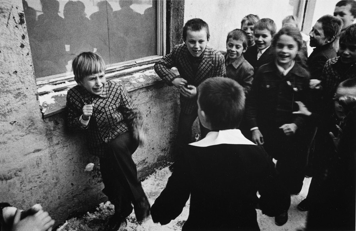 Photograph by Anton Seskus. Children crowd around a peer apparently in a threatening manner. 