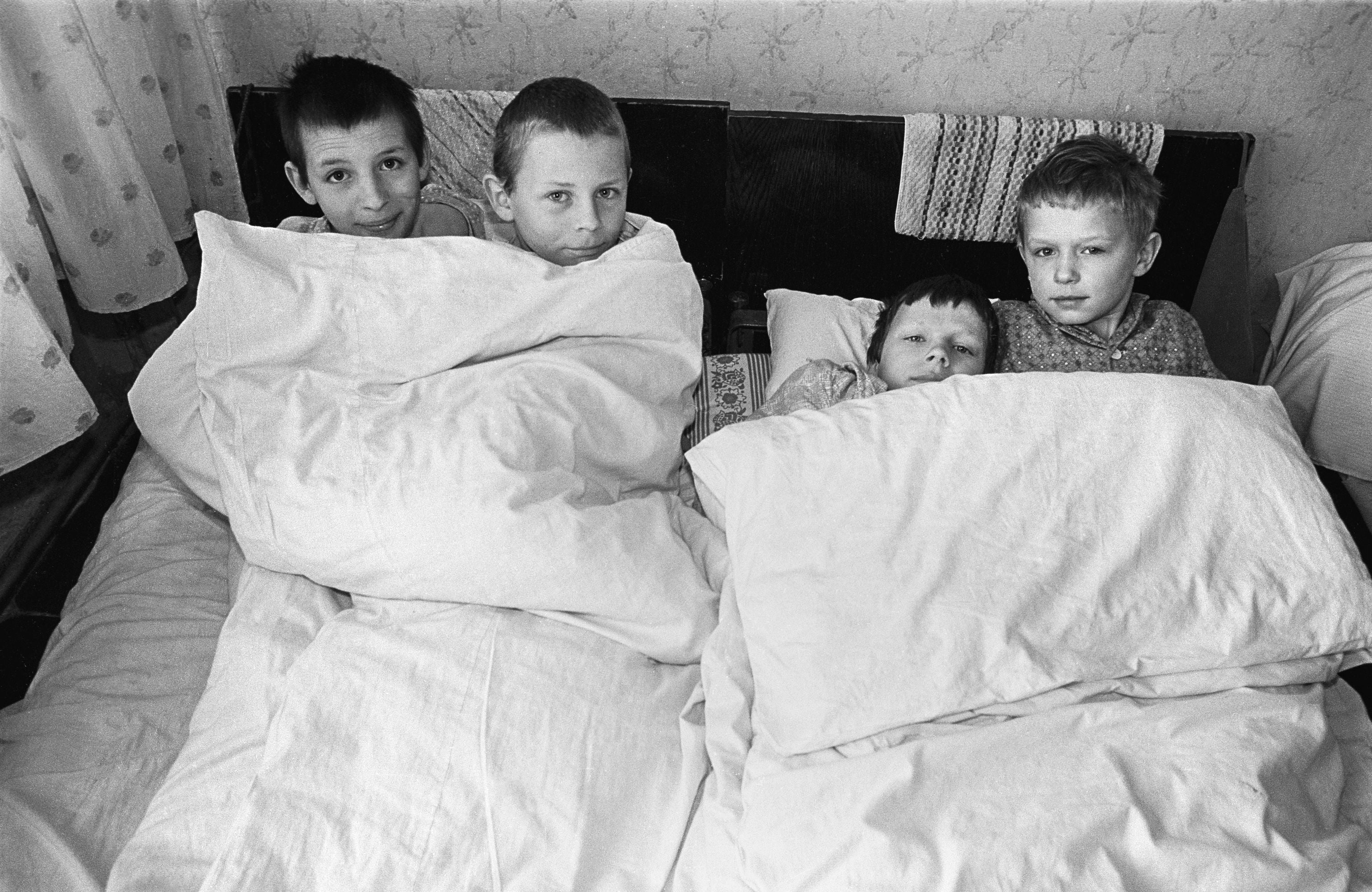 A still from Anton Seskus's photography book. Four children huddle together in a bed. 